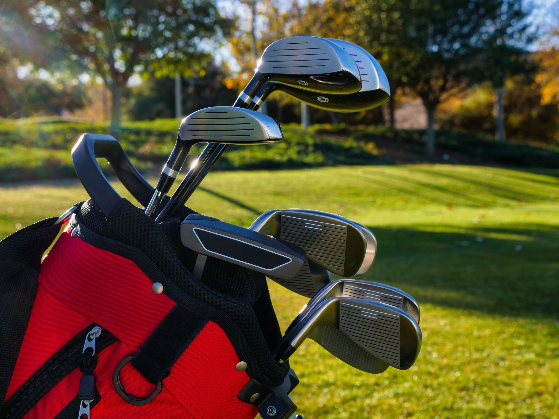 Close-up view of a red golf bag with shiny clubs outdoors on a sunny day.